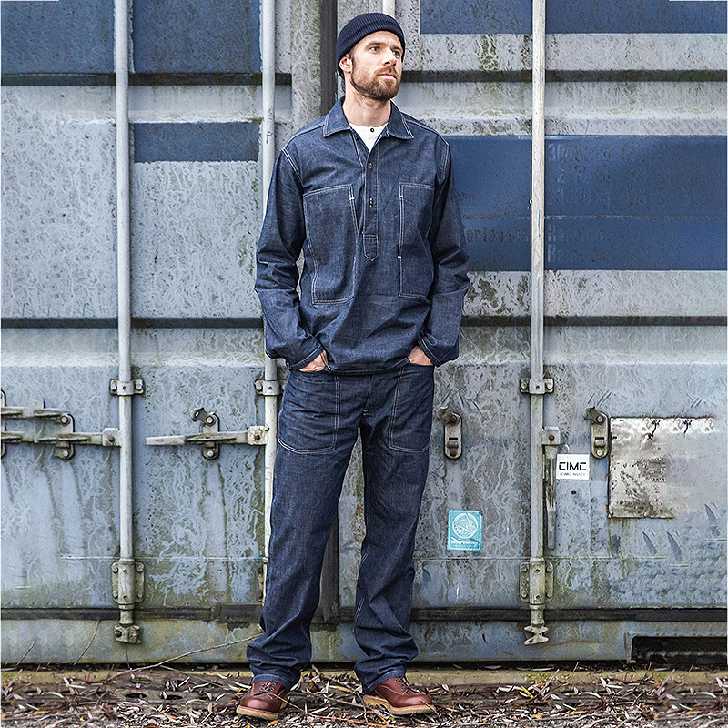 Man wearing a blue work outfit standing in front of a metal container.