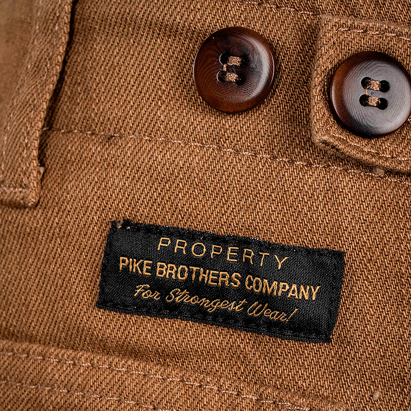 Close-up of a brown OG-107 pant with buttons and a label reading 'Property Pike Brothers Company'.