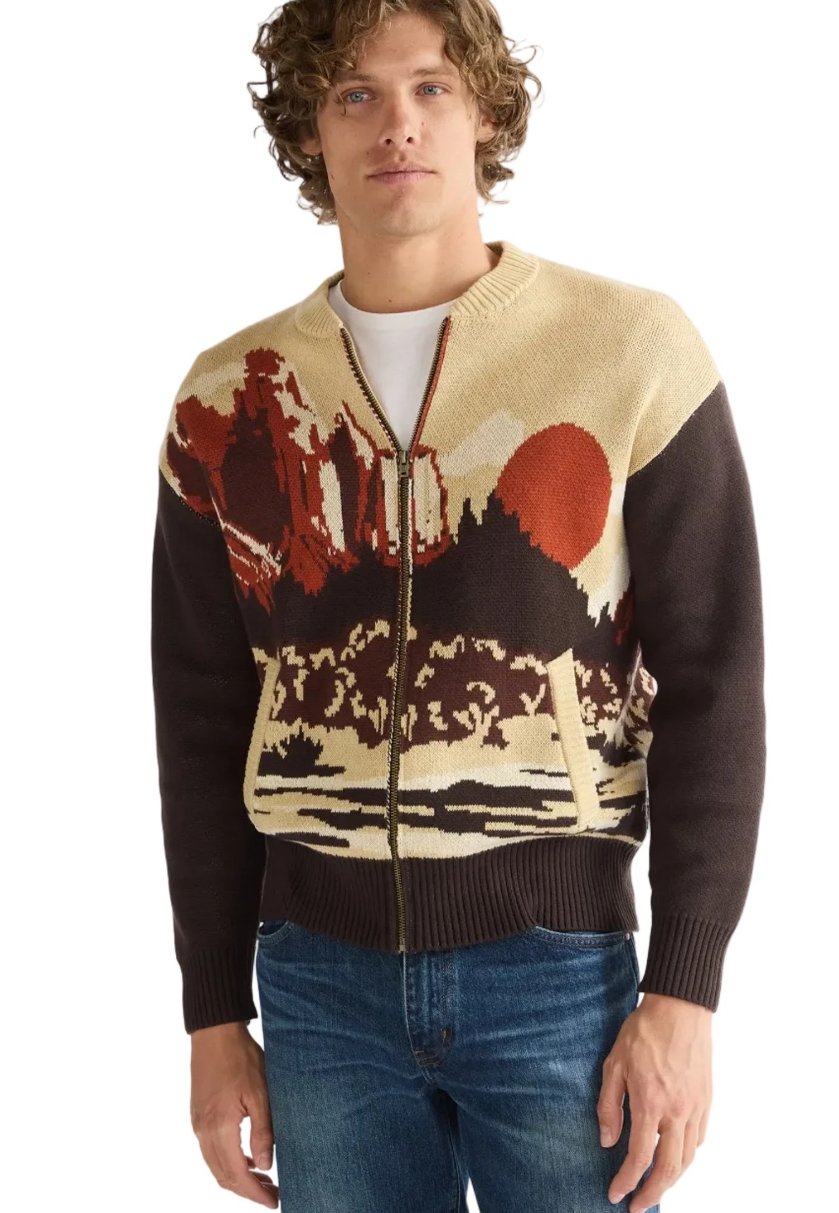 A man wearing a zip-up knit sweater with a scenic landscape pattern in beige, brown, and rust red, paired with blue jeans.