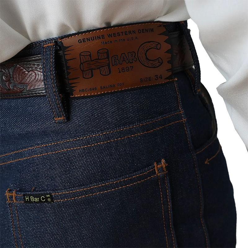 Close-up of blue jeans with a H Bar C belt and label.