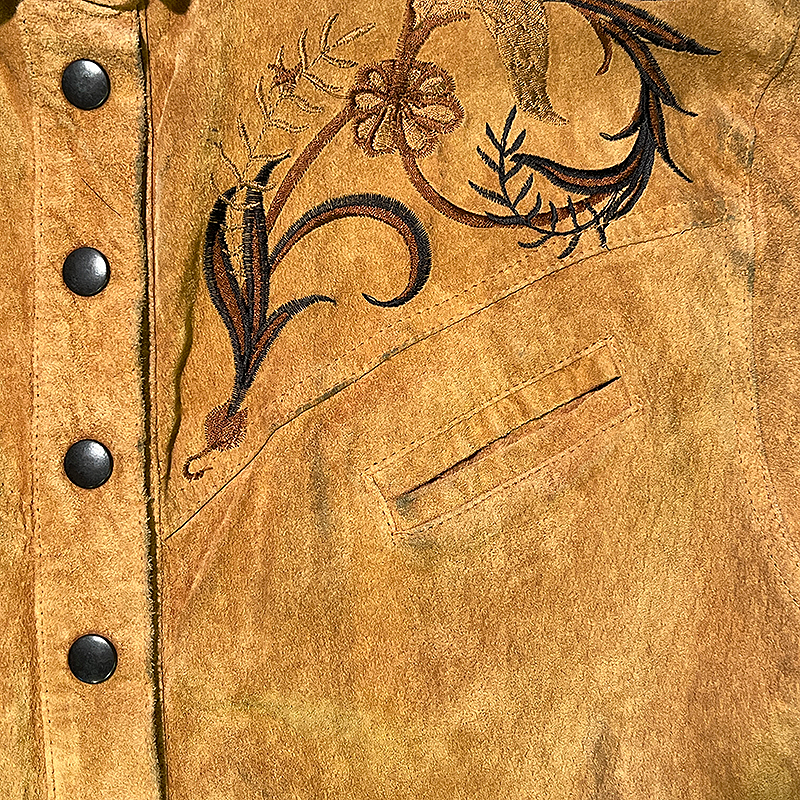 Close-up of a brown western leather shirt with floral embroidery and black buttons.