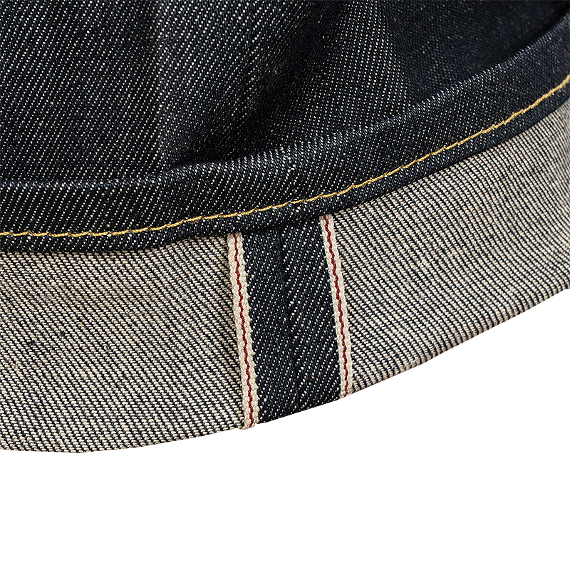 Close-up detail of a folded denim cap brim showing the dark indigo exterior and the lighter gray inner lining with red and white stripe detail characteristic for selvedge denim.