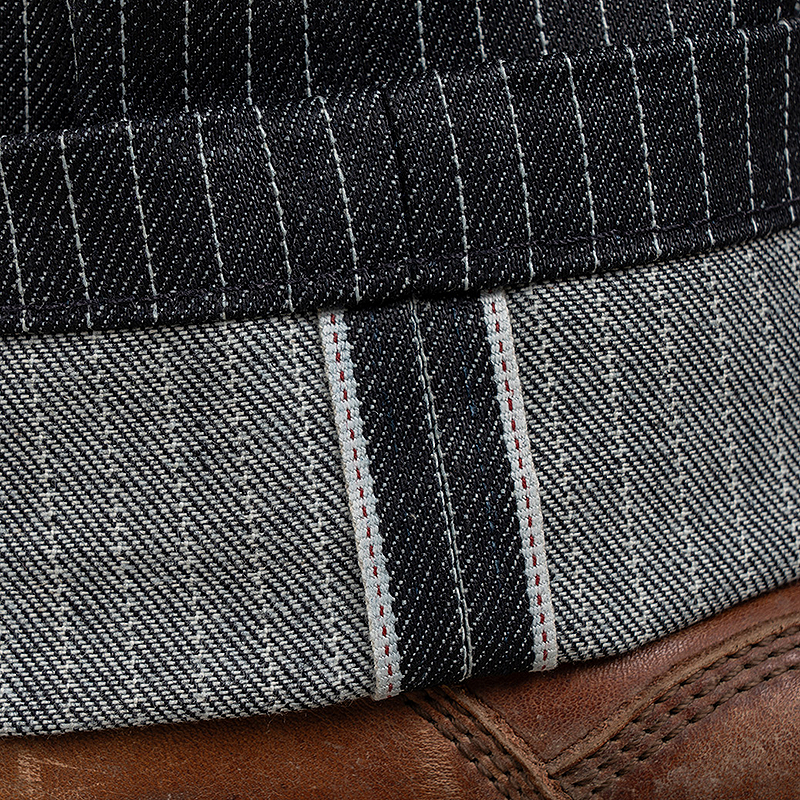 Close-up of folded dark gray and black striped denim fabric with white contrast stitching, shown over a brown leather surface.