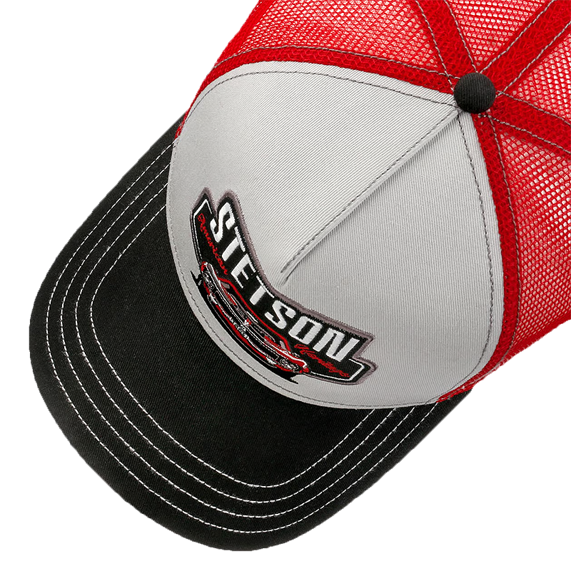 A close-up of a trucker-style cap with a red mesh back, light gray front panels, and a black brim with white contrast stitching. The front panel features a prominent 'STETSON' logo patch with a red car graphic.