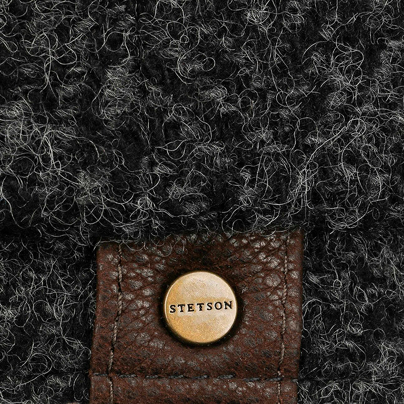 Close-up of a dark brown textured leather strap with a round brass button engraved with the brand name 'STETSON', set against a black and gray fuzzy fabric background.