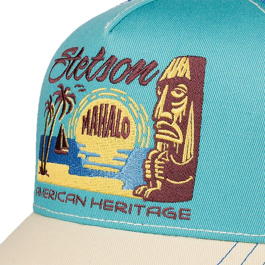 Close-up of a turquoise Stetson Mahalo Trucker Cap with a detailed embroidered graphic on the front panel. The embroidery features a tiki figure, palm trees, a sailboat, a yellow sun, the words 'Stetson' and 'MAHALO', and 'AMERICAN HERITAGE' in maroon.