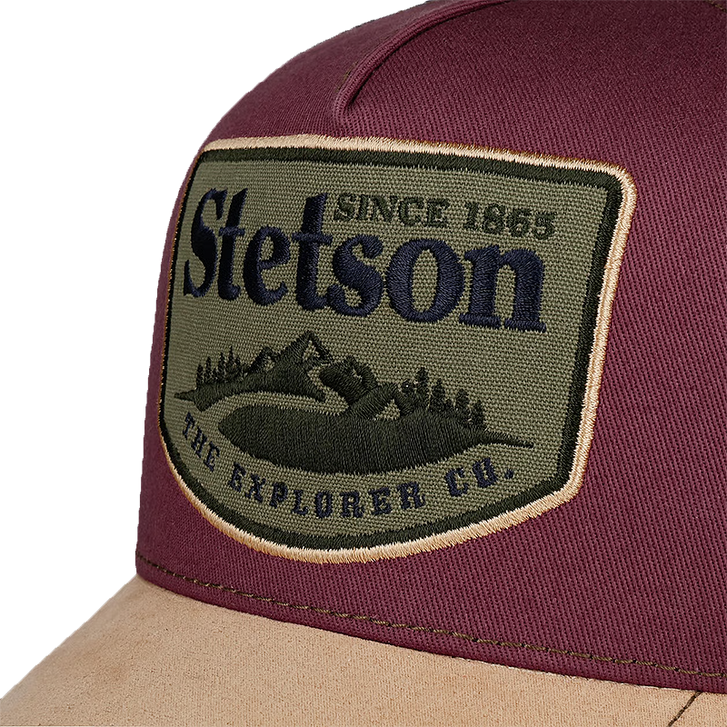Close-up of a Stetson trucker hat featuring a burgundy crown, a tan visor, and a large embroidered Stetson patch on the front.