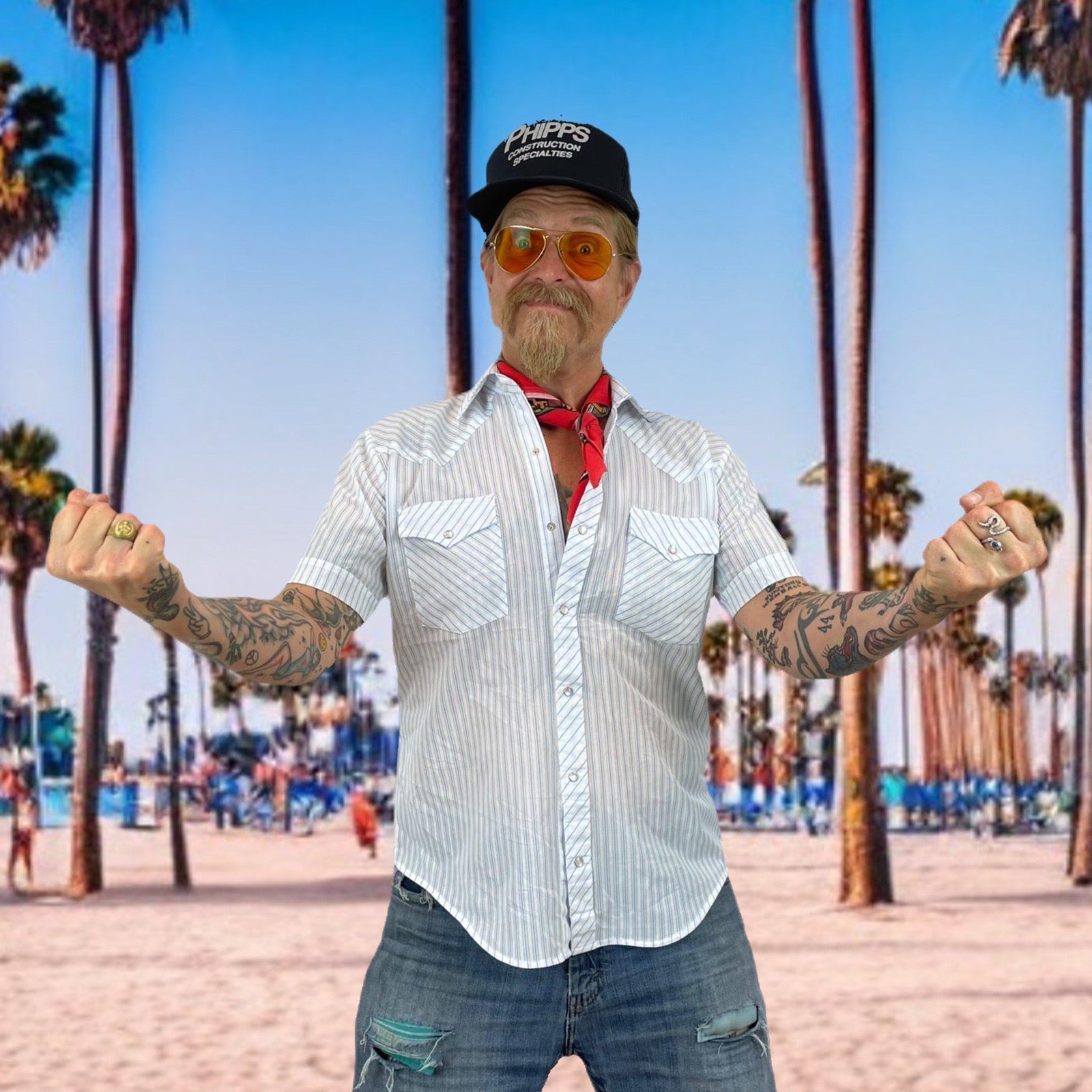 A man with tattoos and a beard wearing a white and gray pinstriped short-sleeve button-down shirt, blue jeans, a red bandana, orange-tinted sunglasses, and a black cap, posing with his arms outstretched against a beach backdrop with palm trees.