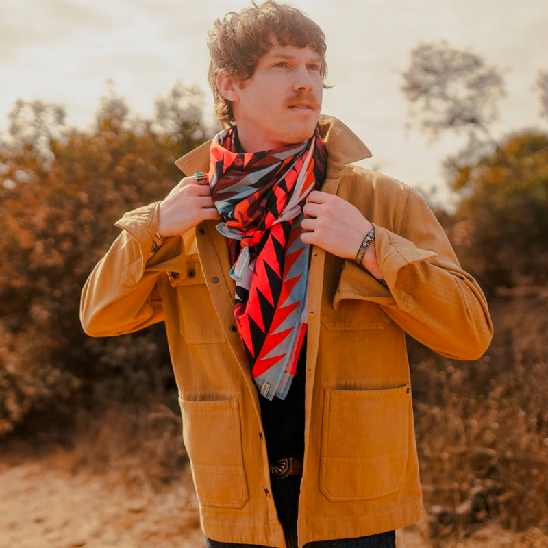 Man wearing a mustard jacket and colorful scarf outdoors with trees in the background